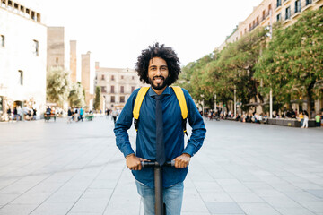 Portrait of smiling man with backpack on his E-Scooter after work, Barcelona, Spain
