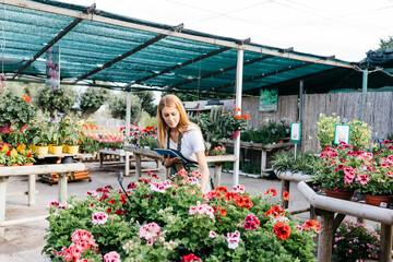 Female worker in a garden center with a tablet caring for flowers