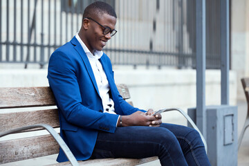 Young businessman wearing blue suit jacket sitting on bench and using smartphone