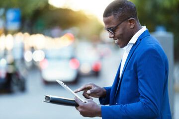 Young businessman wearing blue suit jacket and using his digital tablet at a street