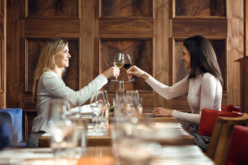 Two businesswomen clinking wine glasses in a restaurant