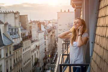France, Paris, portrait of smiling woman on the phone standing on balcony in the evening