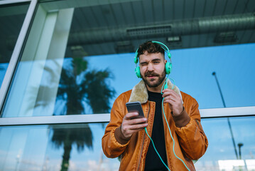 Spain, Cadiz, Young man at the harbour using smartphone, wearing headphones