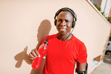 Portrait of man with isotonic drink in sportswear listening music with headphones