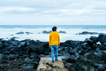 Azores, Sao Miguel, rear view of man looking at the sea from stony coast