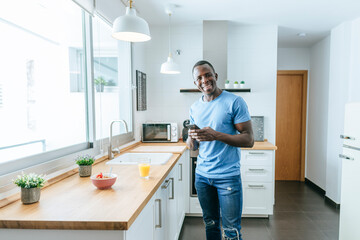 Portrait of happy young man using cell phone in kitchen at home