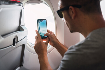 Man in airplane, using smartphone, taking a picture, airplane window