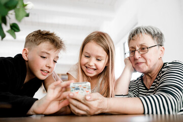 Happy grandmother and grandchildren using cell phone at home