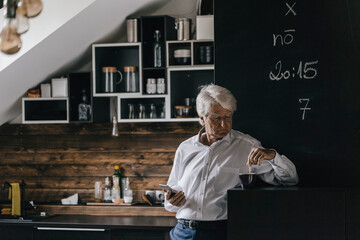 Senior businessman with smartphone and cup of coffee in the kitchen