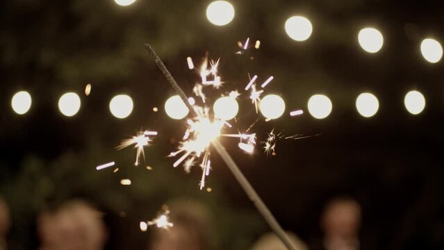 Hand holding Sparkler. Firework sparkler burning with lights in background.