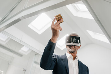Mature businessman in office wearing VR glasses holding Rubik's Cube