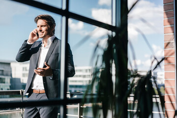 Businessman making a phone call, standing on balcony