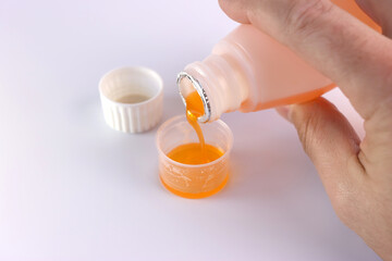 Medicinal syrup is poured into a vessel with liquid volume divisions on a white background....