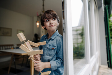 Little boy standing by window, holding self-made toy robot