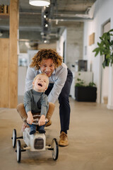 Businessman pushing son on toy car in office