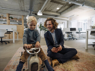 Smiling businessman with son on toy car in office