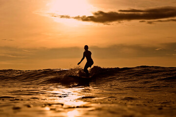 Indonesia, Bali, silhouette of woman surfing at sunset