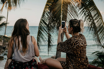Mexico, Quintana Roo, Tulum, two young women with cell phone relaxing on the beach