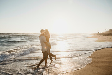 Affectionate young couple hugging at the seashore at sunset
