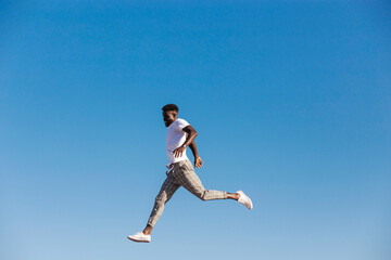 Fototapeta na wymiar Young man jumping against clear blue sky during sunny day