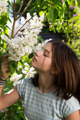 Fototapeta premium Portrait of girl smelling blossom of white lilac