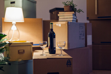 Wine bottle and glasses on cardboard box in an empty room in a new home
