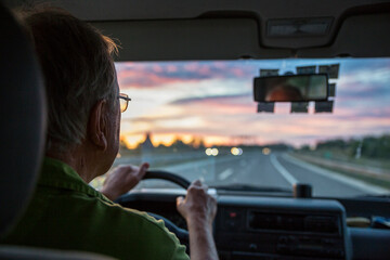 Fototapeta na wymiar Senior man driving a car on a highway at sunset