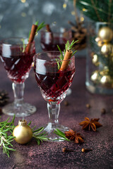 Glasses of red wine in a New Year's atmosphere, garland, lights, spices, Christmas decor. Mulled wine in glasses with rosemary and cinnamon stick.