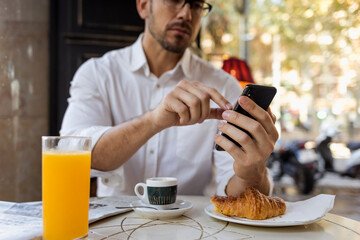 Businessman having breakfast in a cafe and using cell phone