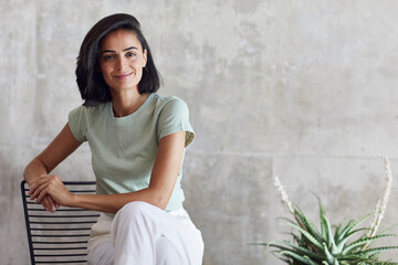 Smiling businesswoman sitting on chair against gray wall in office
