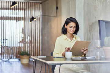 Businesswoman holding clipboard while working at desk in office