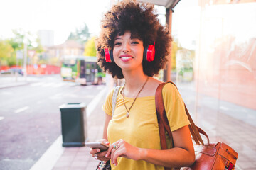 Happy young woman with afro hairdo listening to music with headphones in the city