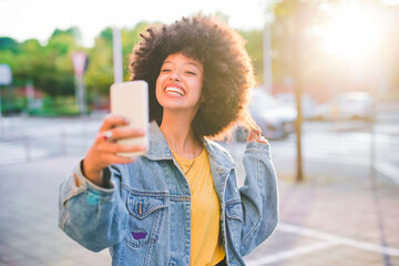 Happy young woman with afro hairdo taking a selfie in the city