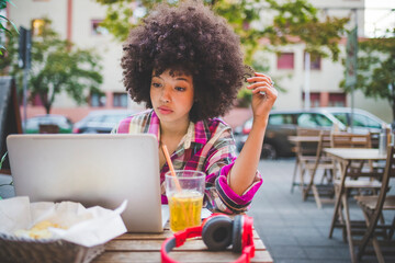 Young woman with afro hairdo using laptop at an outdoor cafe in the city
