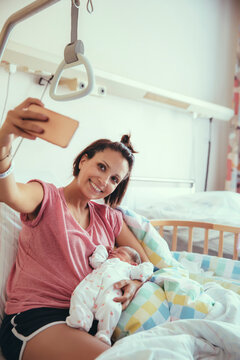 Mother taking a selfie with her newborn baby in hospital bed