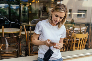 Portrait of woman with protective mask in her hand text messaging in front of a closed coffee shop