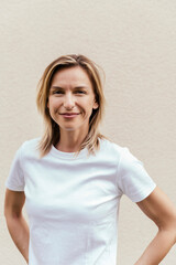 Portrait of smiling blond woman wearing white t-shirt in front of light wall