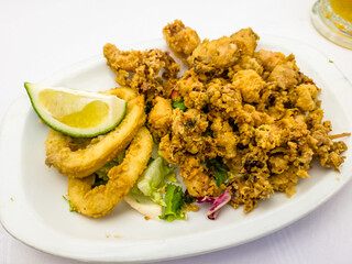 Deep-fried squid with a slice of lime are on a plate on the table in a restaurant