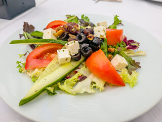 A Greek salad with cucumbers, tomatoes, olives and feta cheese is on a plate in the restaurant