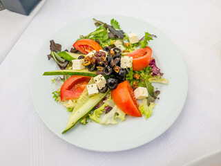 A Greek salad with cucumbers, tomatoes, olives and feta cheese is on a plate in the restaurant