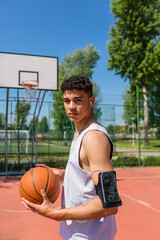 Young man playing basketball, smartphone in arm pocket