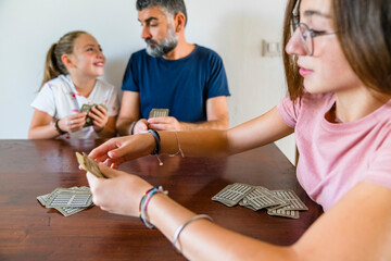 Father with two daughters playing cards on wooden table at home