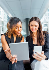 Two businesswomen working with smartphone and tablet in the city