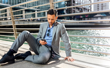 Businessman sitting on a bridge with cell phone in the city