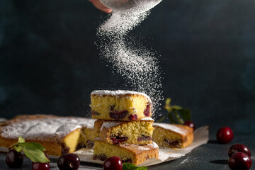 Powdered sugar decorates sponge cake with a cherry on a dark background. Homemade cooking