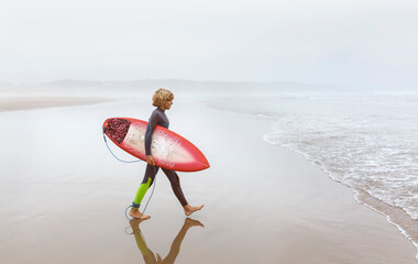 Spain, Aviles, young surfer walking towards the water
