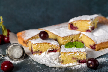 Sponge cake with cherry. Pieces of sliced sponge cake with cherry sprinkled with powdered sugar on a gray background