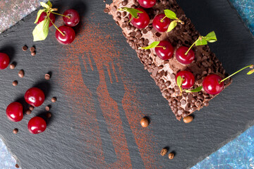 Chocolate roll cake with cream and cherries on a dark background. Top view
