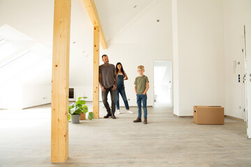 Parents with son standing on hardwood floor in attic of new unfurnished home