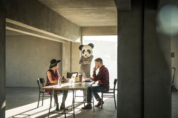 Fototapeta na wymiar Woman with panda mask watching colleagues in office